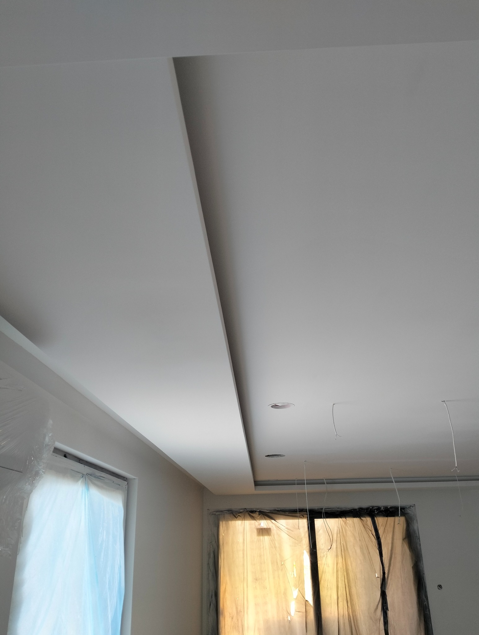 Nowoczesny sufit podwieszany z oświetleniem punktowym, widok z dołu. Okna zabezpieczone folią malarską. Minimalistyczny design, świeżo po remoncie.