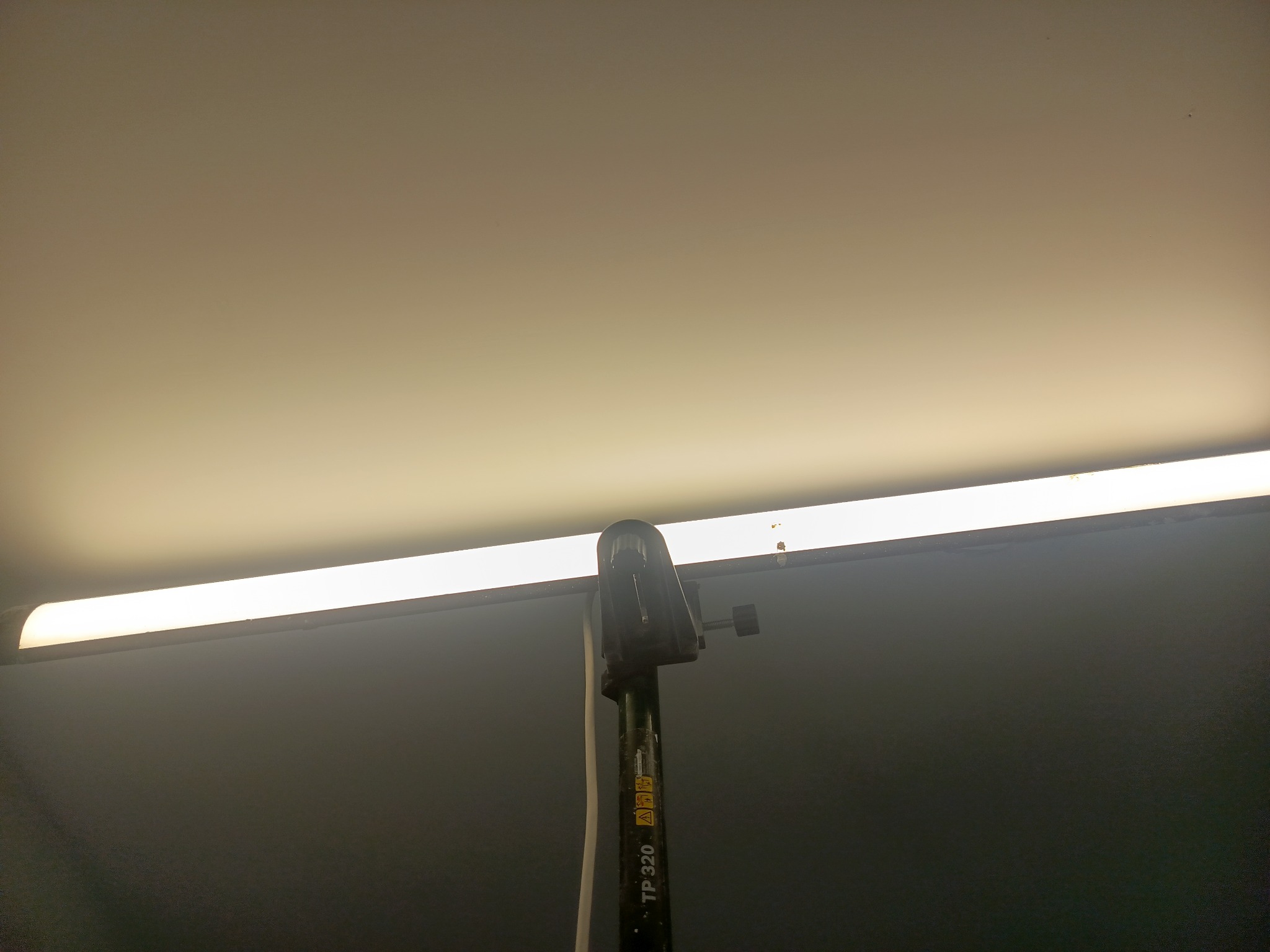 Lampa LED na statywie oświetlająca szarą ścianę i sufit. Widoczne zabrudzenia na suficie. Ujęcie od dołu, z bliska.