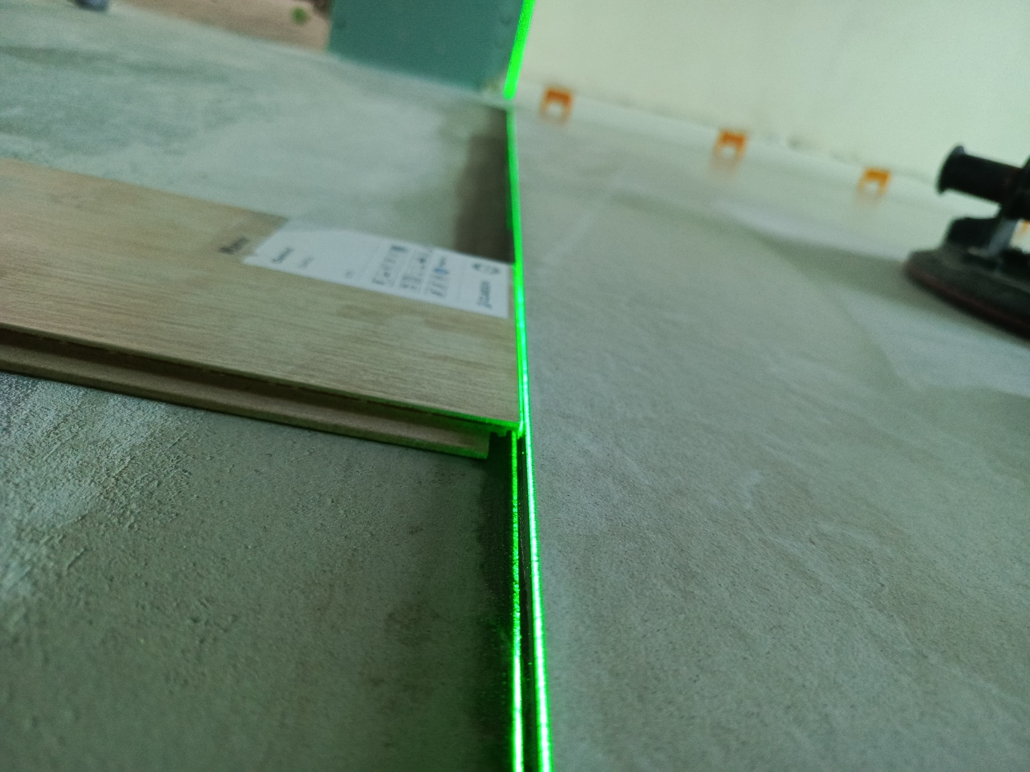 Układanie paneli podłogowych z użyciem lasera, widoczne panele i narzędzia. Precyzyjne wyznaczanie linii cięcia. Detal z bliska.