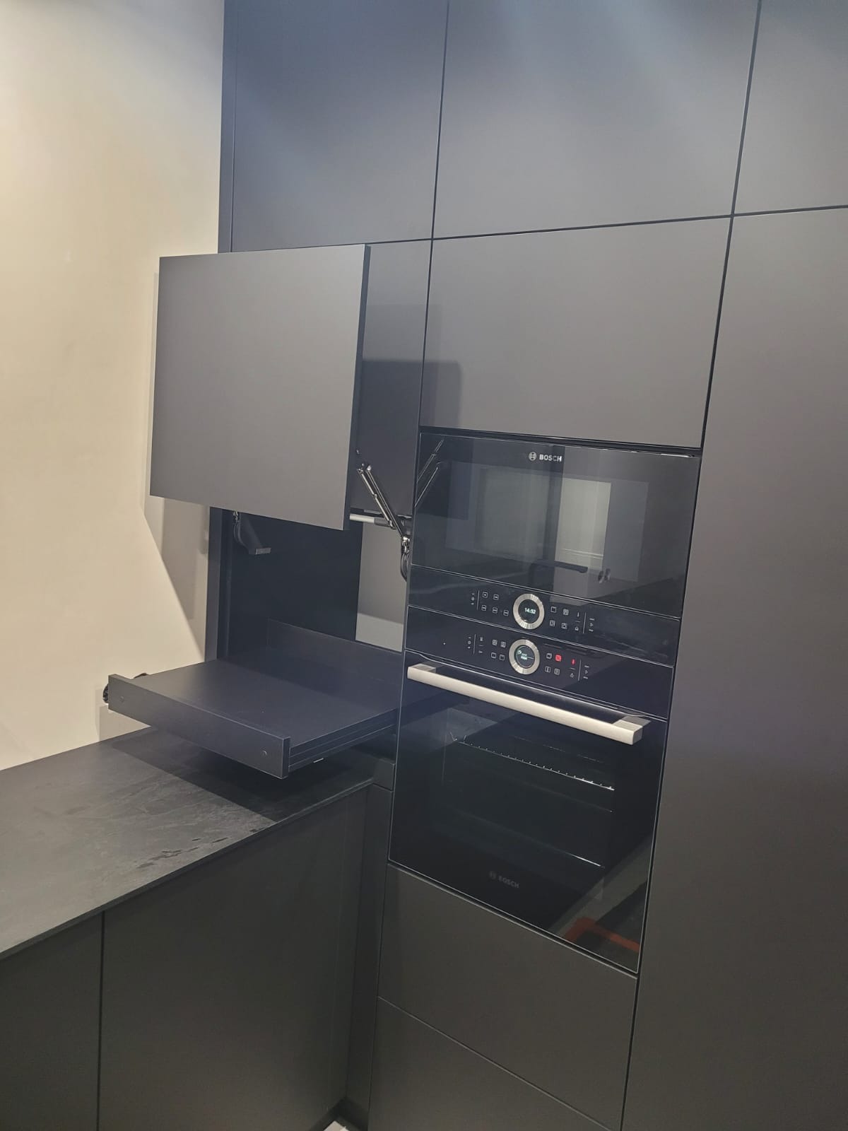 Nowoczesna, szara zabudowa kuchenna z piekarnikiem Bosch i wysuwanym blatem. Minimalistyczny design, fronty bez uchwytów, oświetlenie punktowe.