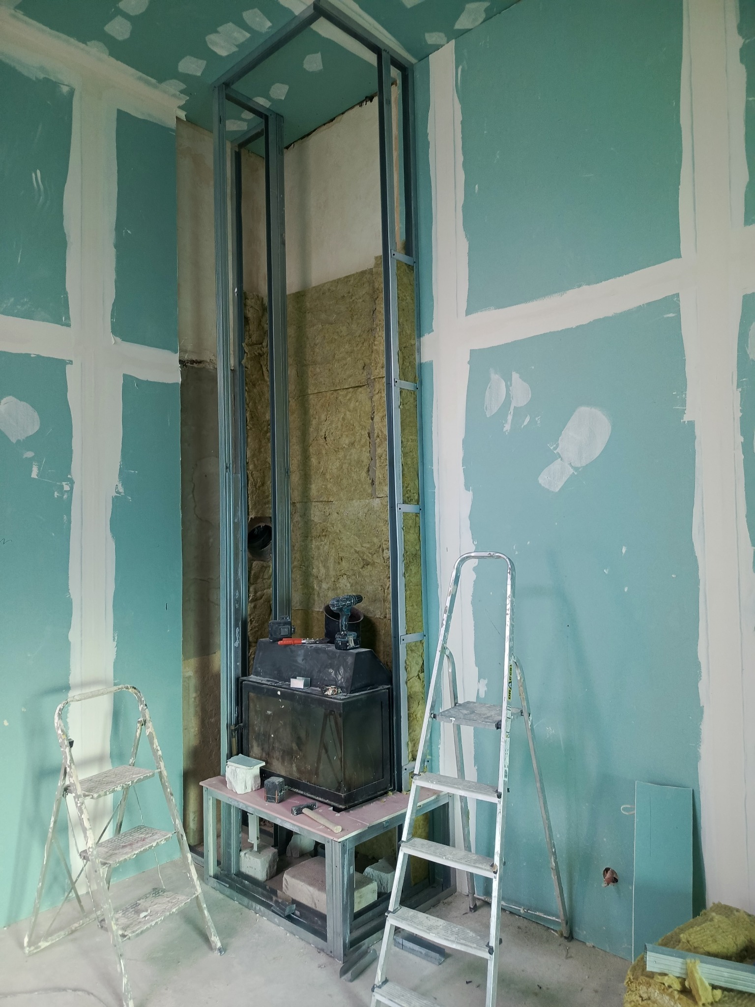 Wnętrze w trakcie prac wykończeniowych: ściany z płyt gipsowo-kartonowych, metalowa konstrukcja, ocieplenie z wełny mineralnej, drabiny i narzędzia.