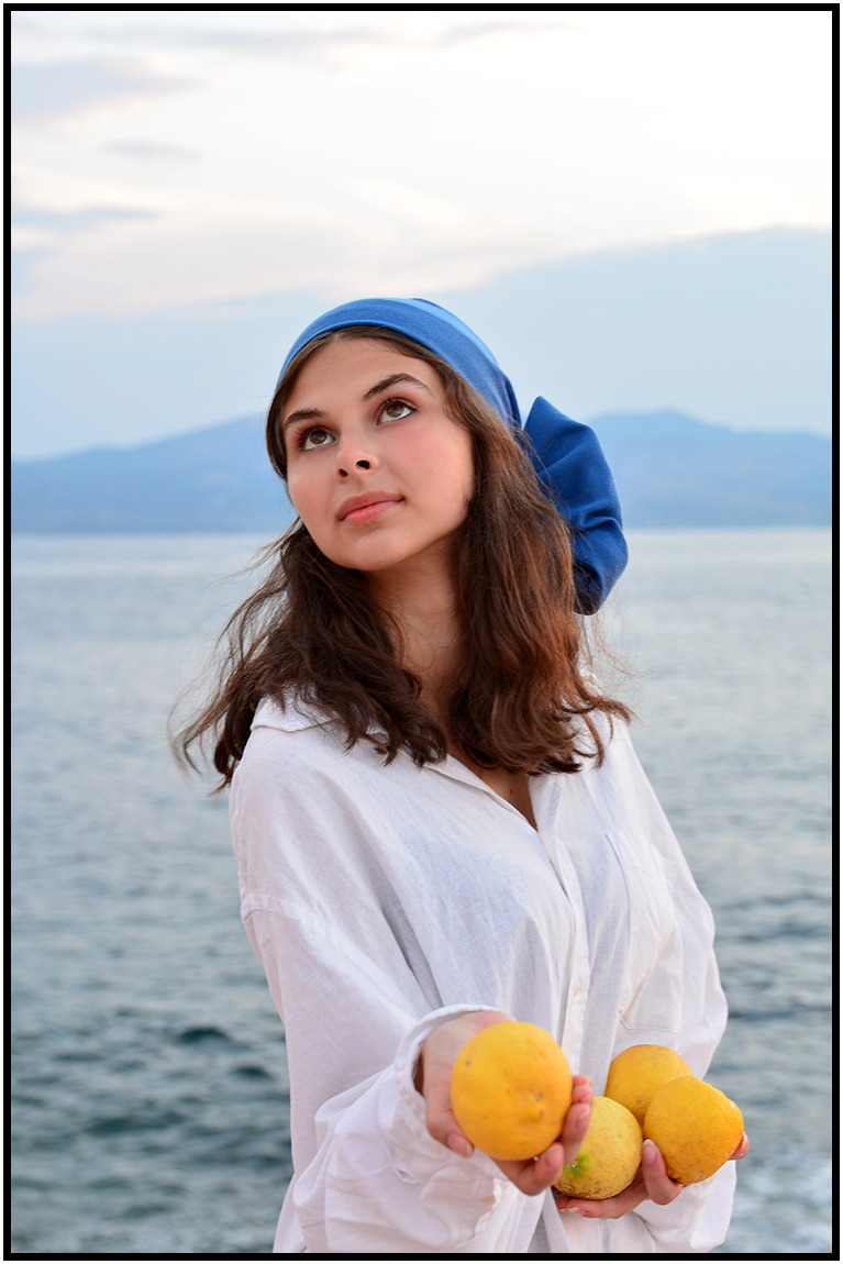 Portret młodej kobiety w błękitnej chuście, trzymającej cytryny na tle morza i gór, w stylu nawiązującym do malarstwa dawnych mistrzów.
