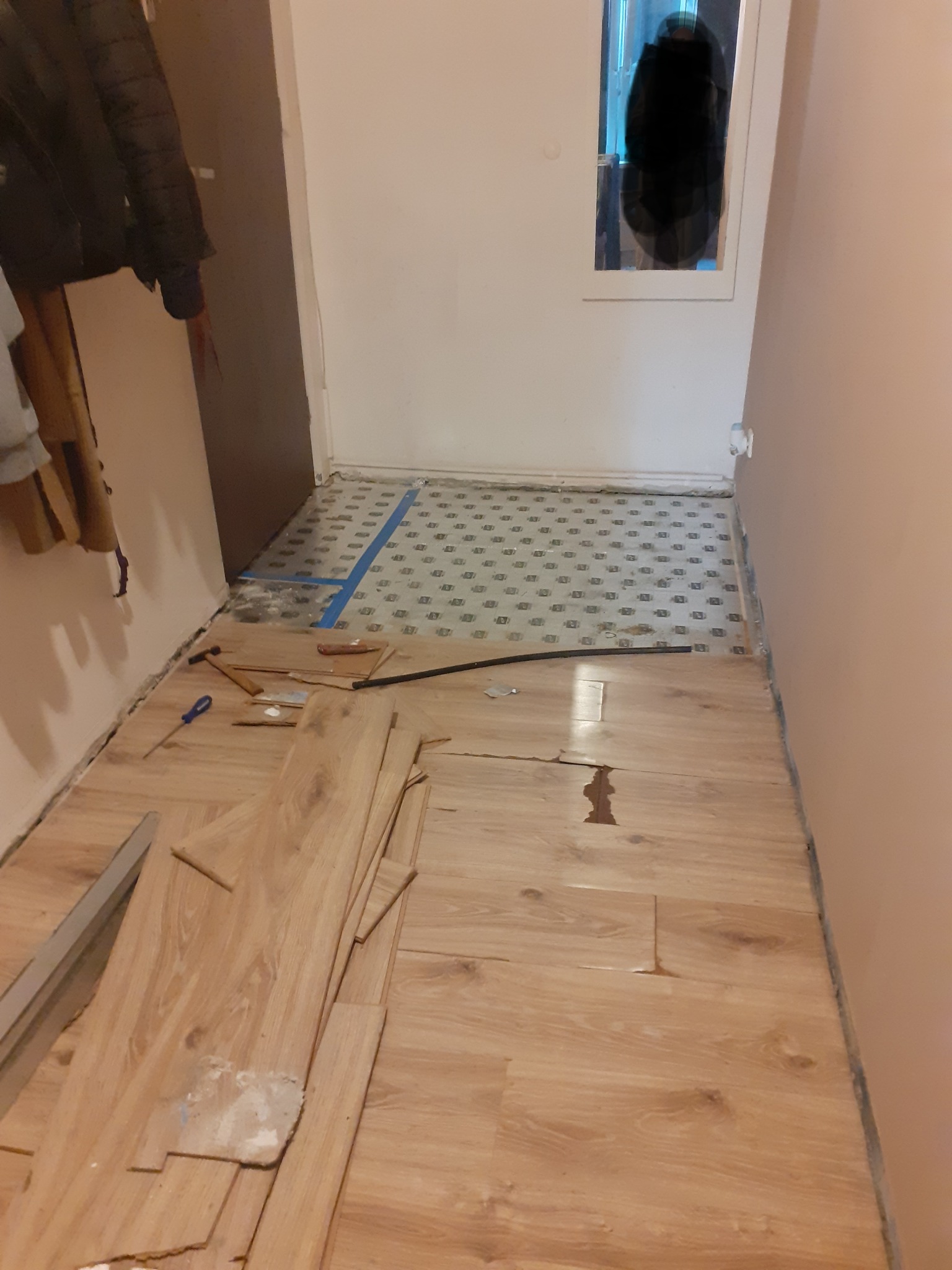 Układanie paneli podłogowych w korytarzu, widoczne narzędzia i niedokończona praca. Stare płytki pod częściowo ułożonymi panelami.