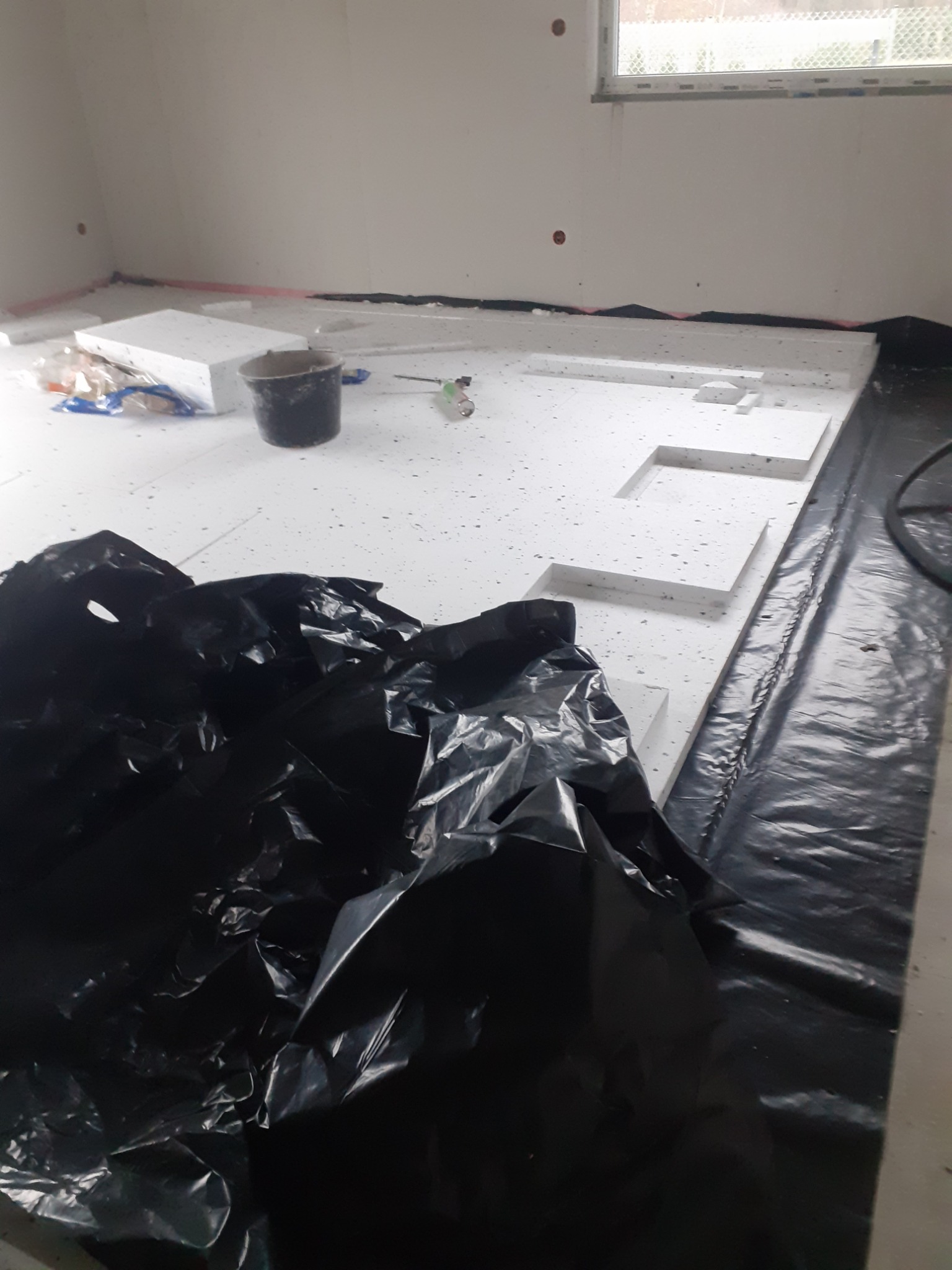 Układanie styropianu pod wylewkę w Chorzowie. Czarna folia izolacyjna, białe płyty styropianowe, przygotowanie podłoża pod ogrzewanie podłogowe.