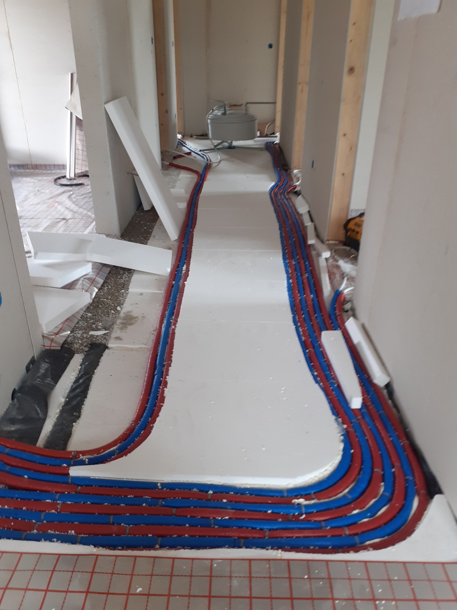Montaż ogrzewania podłogowego: rury grzewcze ułożone na izolacji w korytarzu, przygotowane do zalania wylewką. Widoczne detale instalacji i materiałów budowlanych.