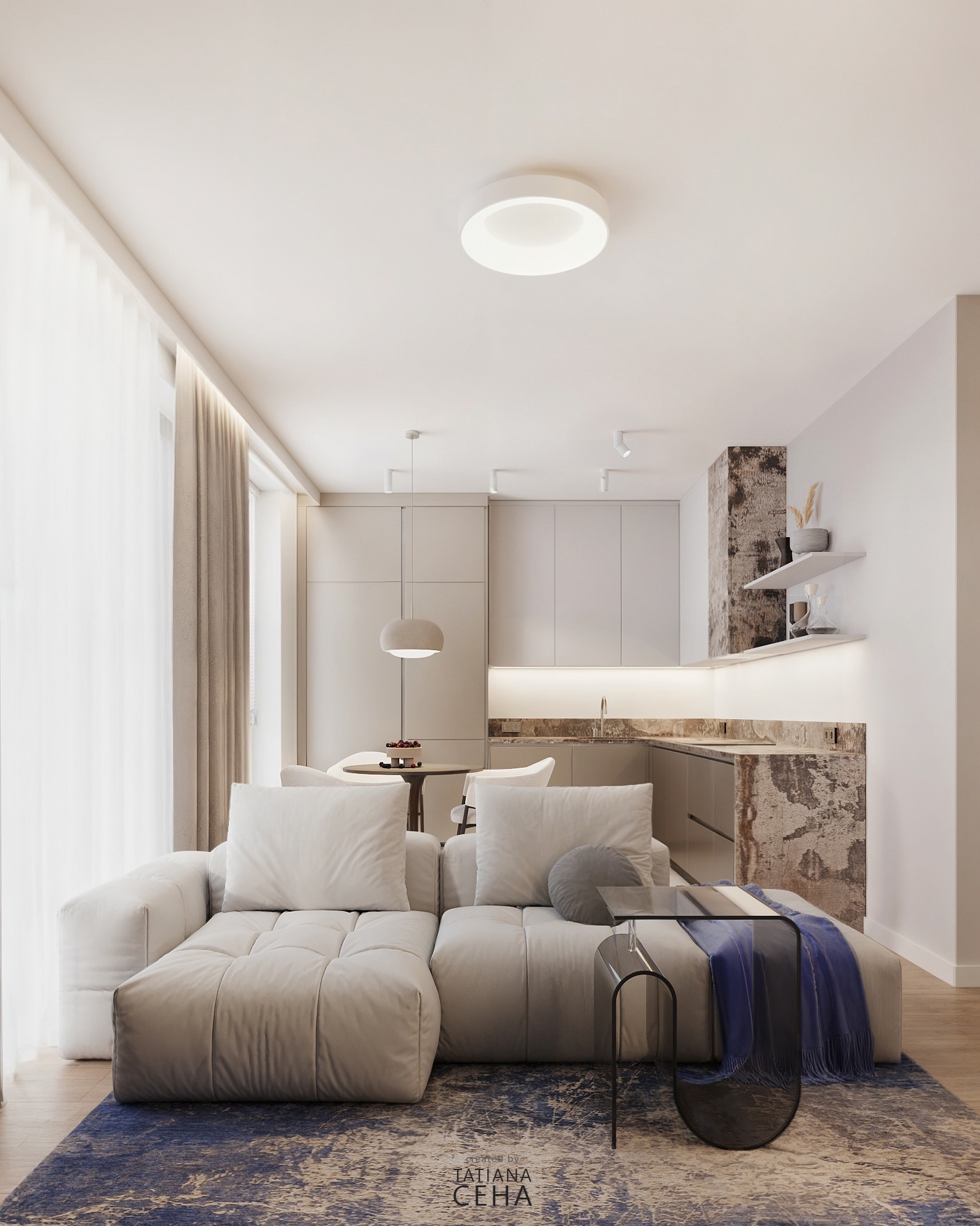 Jasne wnętrze: kremowy narożnik z poduszkami, szklany stolik z niebieskim pledem na wzorzystym dywanie. W tle aneks kuchenny i okno z zasłonami.