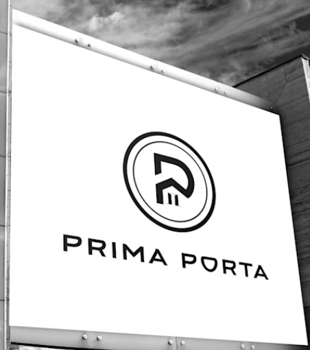 Czarno-białe zdjęcie tablicy reklamowej z okrągłym logo i nazwą 'PRIMA PORTA' na tle pochmurnego nieba i fragmentu budynku, widziana z dołu pod kątem.