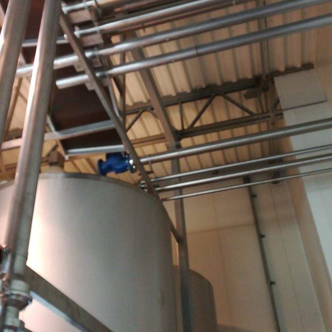 Metalowa konstrukcja wsporcza z rurami i zbiornikiem z niebieskim zaworem, widok z dołu, oświetlenie przemysłowe.