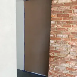 Ściana po nałożeniu gładzi, zabezpieczona taśmą malarską, sąsiadująca z czerwoną ścianą z cegły. Widoczny fragment białej, wykończonej ściany w tle.
