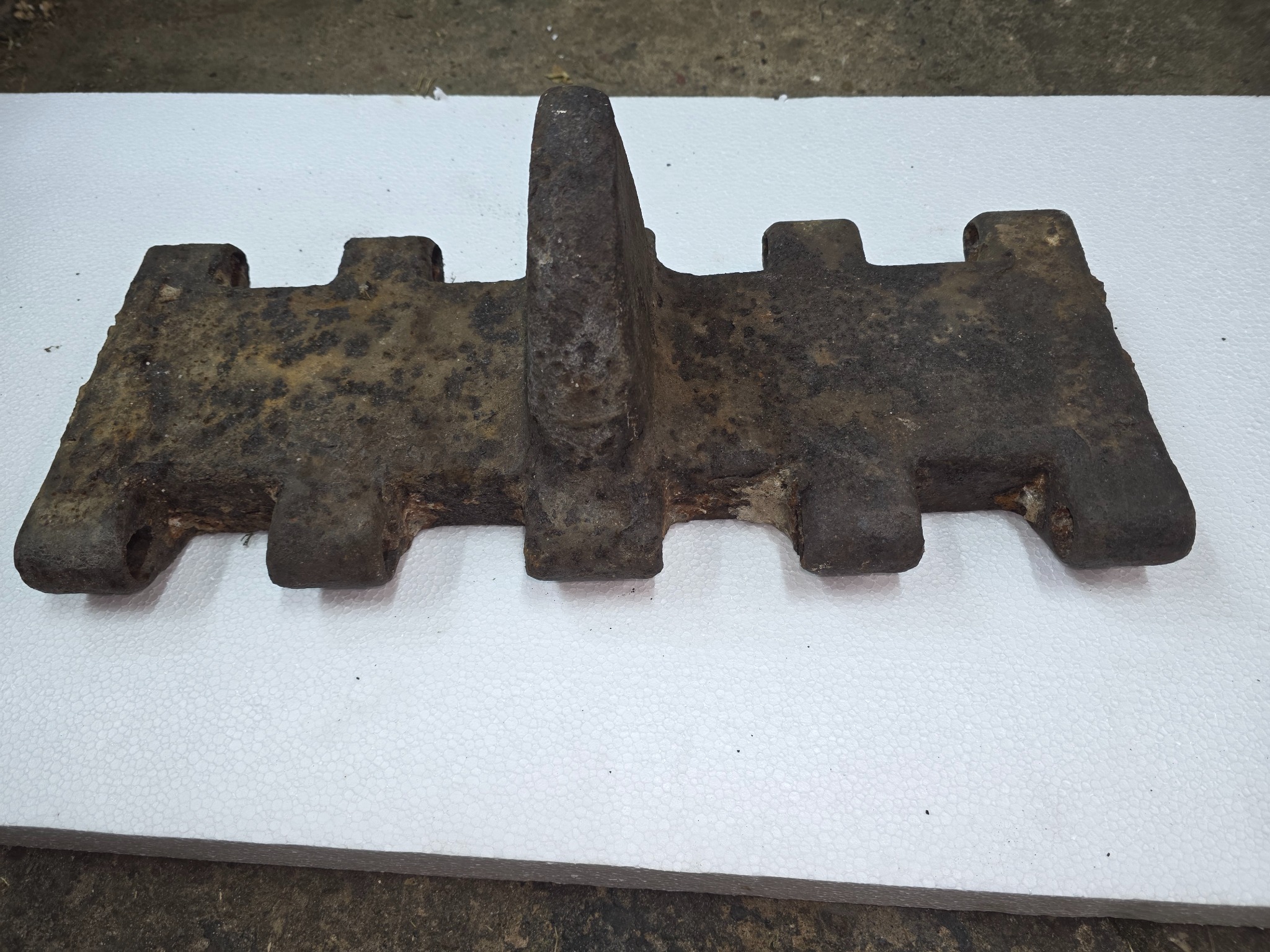 Zardzewiały element gąsienicy czołgu na białym styropianie. Widoczne ślady korozji i zabrudzenia. Detal po piaskowaniu, ukazujący usunięcie rdzy i przygotowanie do dalszej obróbki.