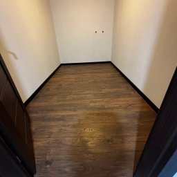 Paweł Kwaśny - Ukończona podłoga z paneli w małym pomieszczeniu o nietypowym kształcie, widok z góry, ciemne listwy przypodłogowe, ściany w odcieniach bieli, widoczne otwory na gniazdka.