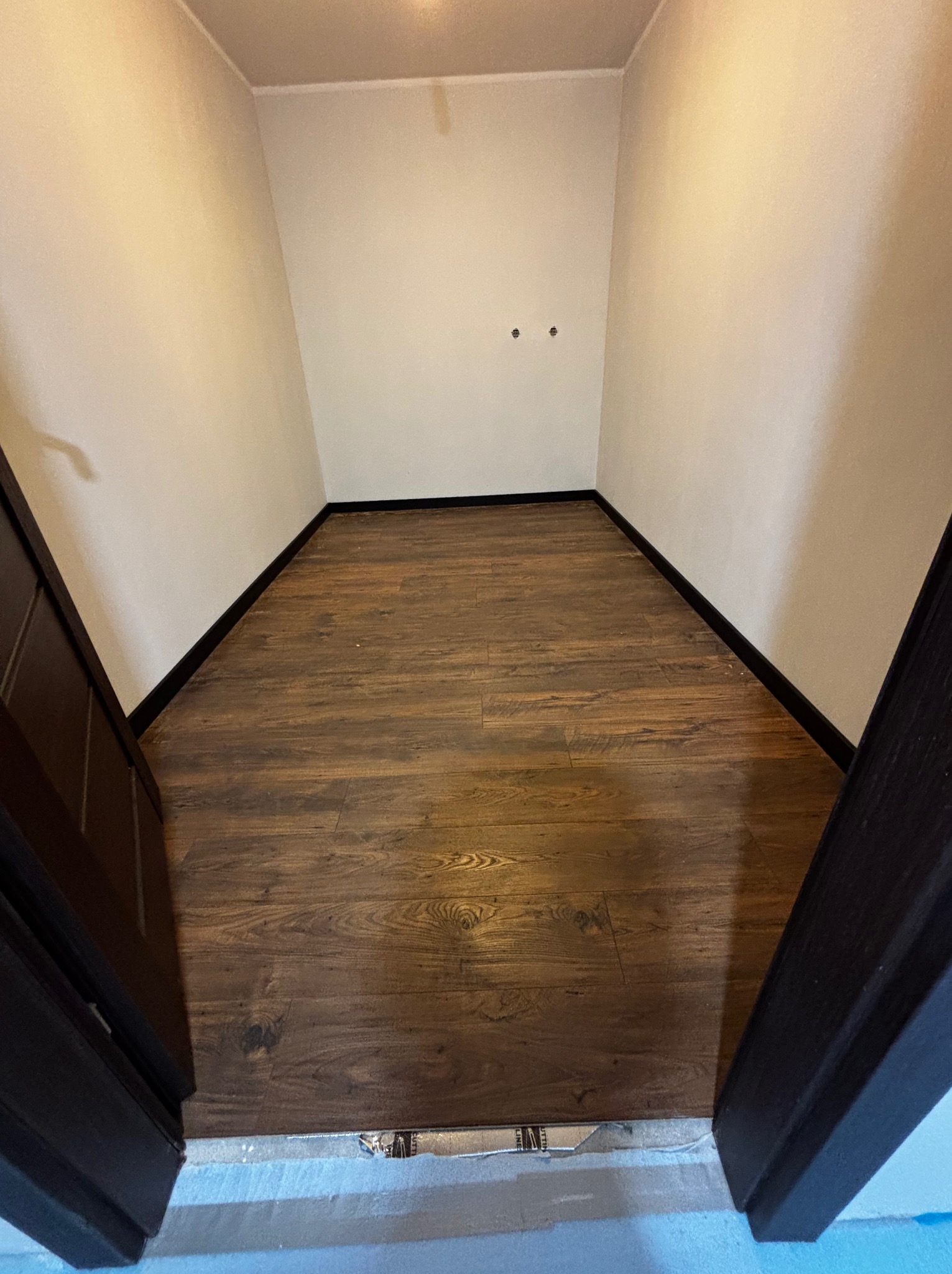 Ukończona podłoga z paneli w małym pomieszczeniu o nietypowym kształcie, widok z góry, ciemne listwy przypodłogowe, ściany w odcieniach bieli, widoczne otwory na gniazdka.