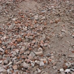 Trans-Janda s. c. Jakub Janda Bartosz Janda - Góra gruzu ceglanego i kamiennego z domieszką ziemi, widoczna faktura i kolory materiałów. Fotografia z bliska, ukazująca detale.