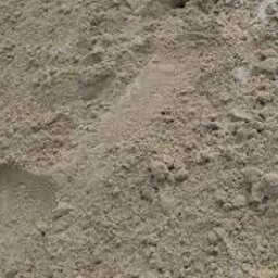 Trans-Janda s. c. Jakub Janda Bartosz Janda - Góra piasku o drobnej granulacji, widoczne ślady butów. Jasny, naturalny odcień, delikatne cienie podkreślają teksturę. Część piasku na betonowej powierzchni.