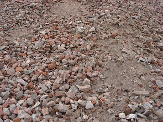 Góra gruzu ceglanego i kamiennego z domieszką ziemi, widoczna faktura i kolory materiałów. Fotografia z bliska, ukazująca detale.