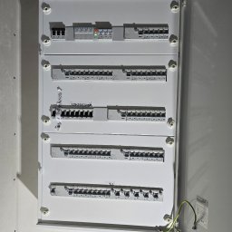 ADAM BREMER Activa Electric - Otwarta, biała skrzynka elektryczna Eaton z bezpiecznikami i naklejkami z opisami obwodów. Widoczne przewody uziemiające i fragment ściany.