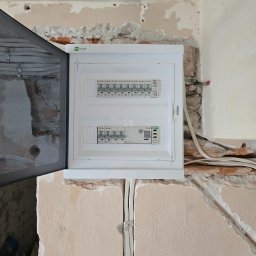 ADAM BREMER Activa Electric - Rozdzielnia elektryczna EATON w trakcie montażu, widoczne kable i surowy stan ściany. Otwarta obudowa ukazuje zabezpieczenia.