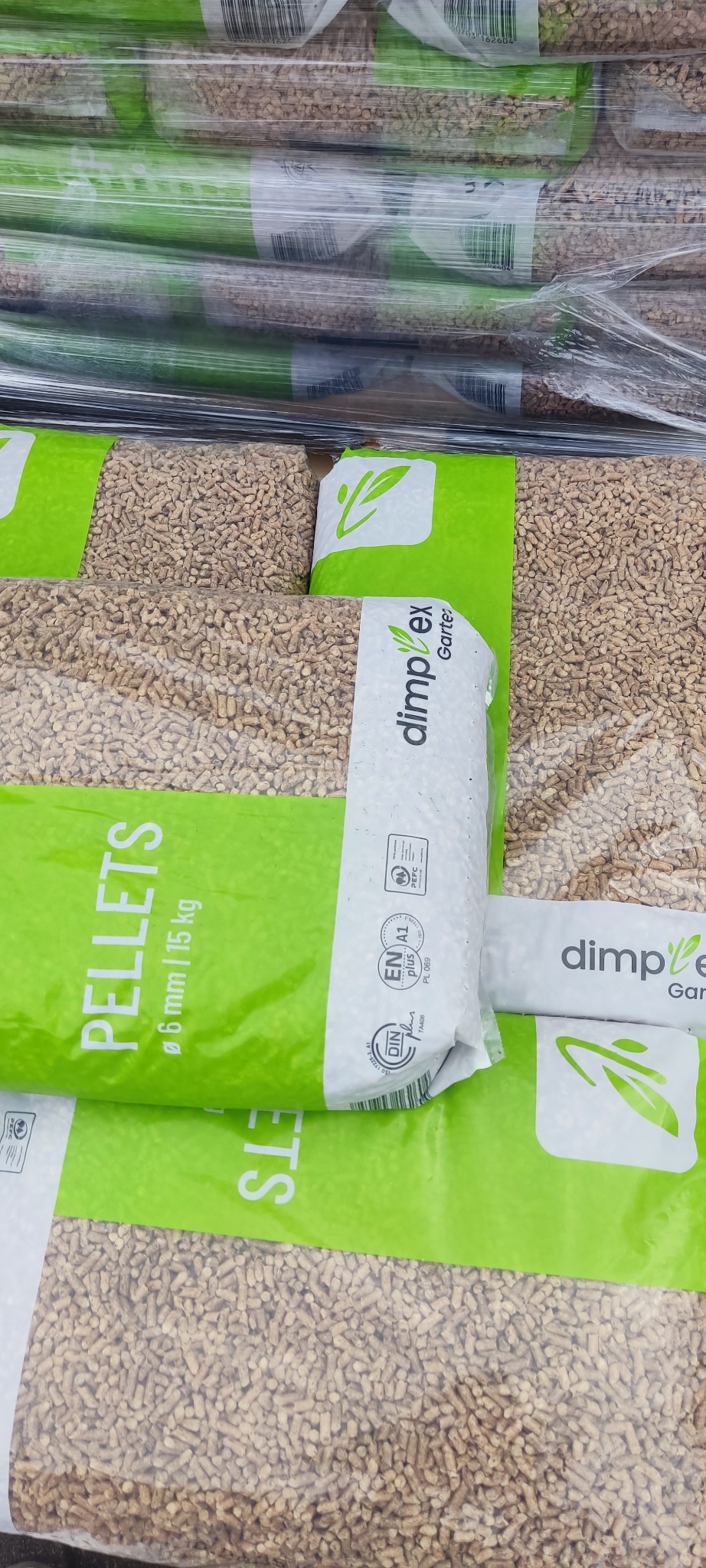 Szereg worków z pelletem drzewnym, marki Dimplex Garte, o średnicy 6 mm i wadze 15 kg, ułożonych jeden na drugim. Część worków jest zapakowana w folię.