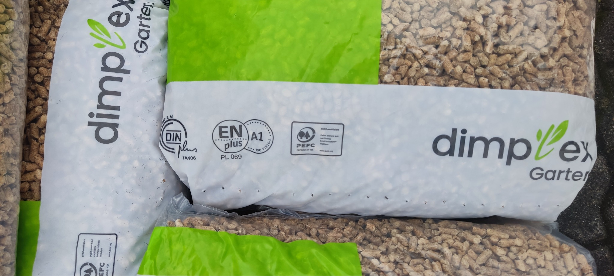 Worki z pelletem drzewnym marki Dimplex Garten, z certyfikatami DINplus, ENplus A1 i PEFC. Widoczne drewniane granulki w przezroczystym opakowaniu.