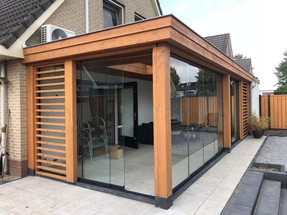 Zabudowa tarasu z drewna i szkła, z przesuwnymi panelami szklanymi i drewnianymi lamelami, widok z zewnątrz na jasną podłogę i część domu.