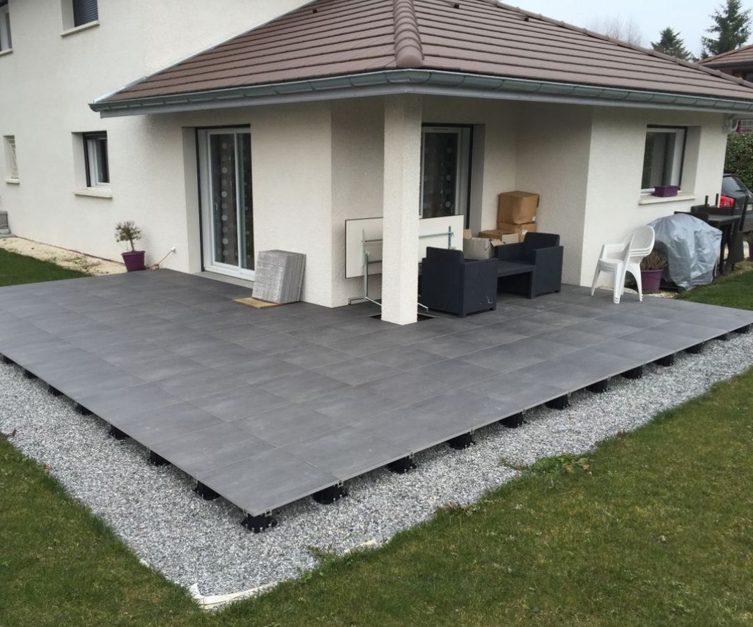 Nowoczesny taras z szarych płyt na regulowanych wspornikach, otoczony żwirem, przylegający do domu w Żukowie. Widoczne meble ogrodowe.
