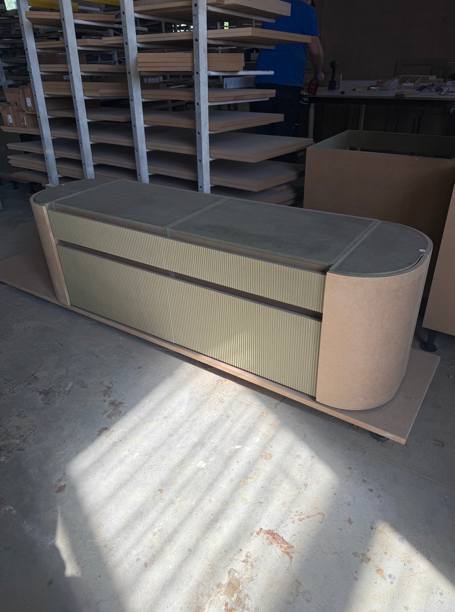 Nowoczesna konsola z ryflowanymi frontami szuflad w odcieniach beżu, w trakcie produkcji w warsztacie stolarskim, z widocznymi materiałami i półkami w tle.