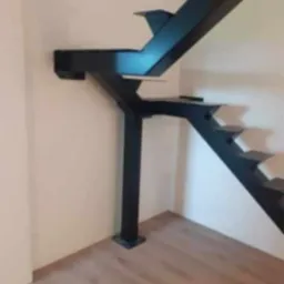 Nowoczesne, czarne schody metalowe wspornikowe, przymocowane do ściany, z widoczną konstrukcją nośną i drewnianą podłogą. Minimalistyczny design.