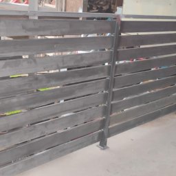 PIOTR-SPAW - Nowoczesne, poziome ogrodzenie metalowe w surowym wykończeniu, z widocznymi spawami i minimalistycznym designem. Elementy mocujące widoczne u dołu.