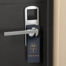 Hotelowa zawieszka na klamce z logo 'Oasis Resort' w kolorze złotym na granatowym tle. Drzwi z ciemnego drewna z metalową klamką i zamkiem elektronicznym.