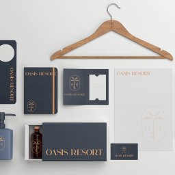 MAKX Projektowanie Graficzne - Komplet materiałów identyfikacji wizualnej dla Oasis Resort: wizytówka, papier firmowy, zawieszka na drzwi, kosmetyki i drewniany wieszak z logo w kolorach granatu i złota.
