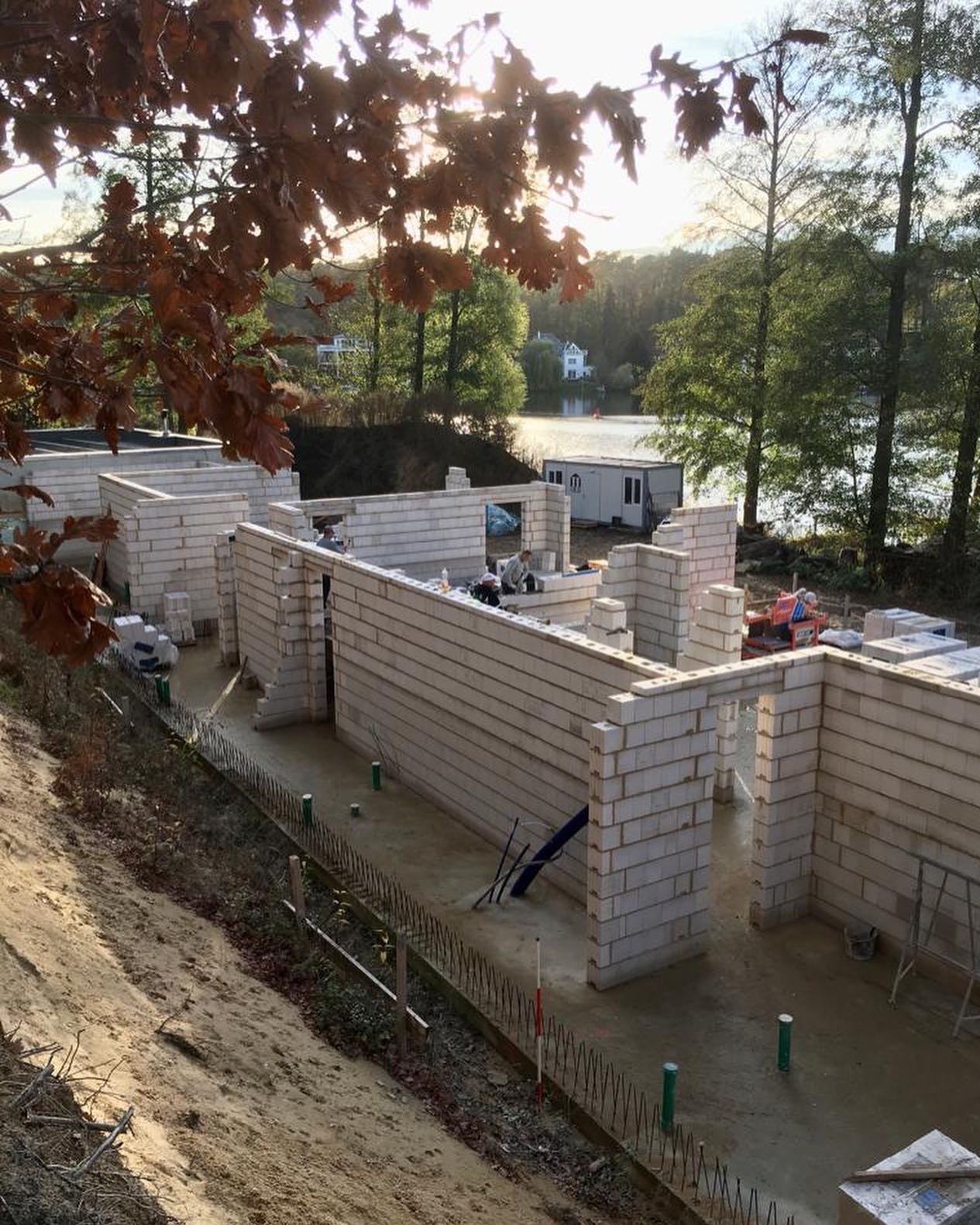 Wznoszenie murów z bloczków betonu komórkowego na budowie domu jednorodzinnego, widok z góry, w tle jezioro i drzewa, jesienne liście w kadrze.