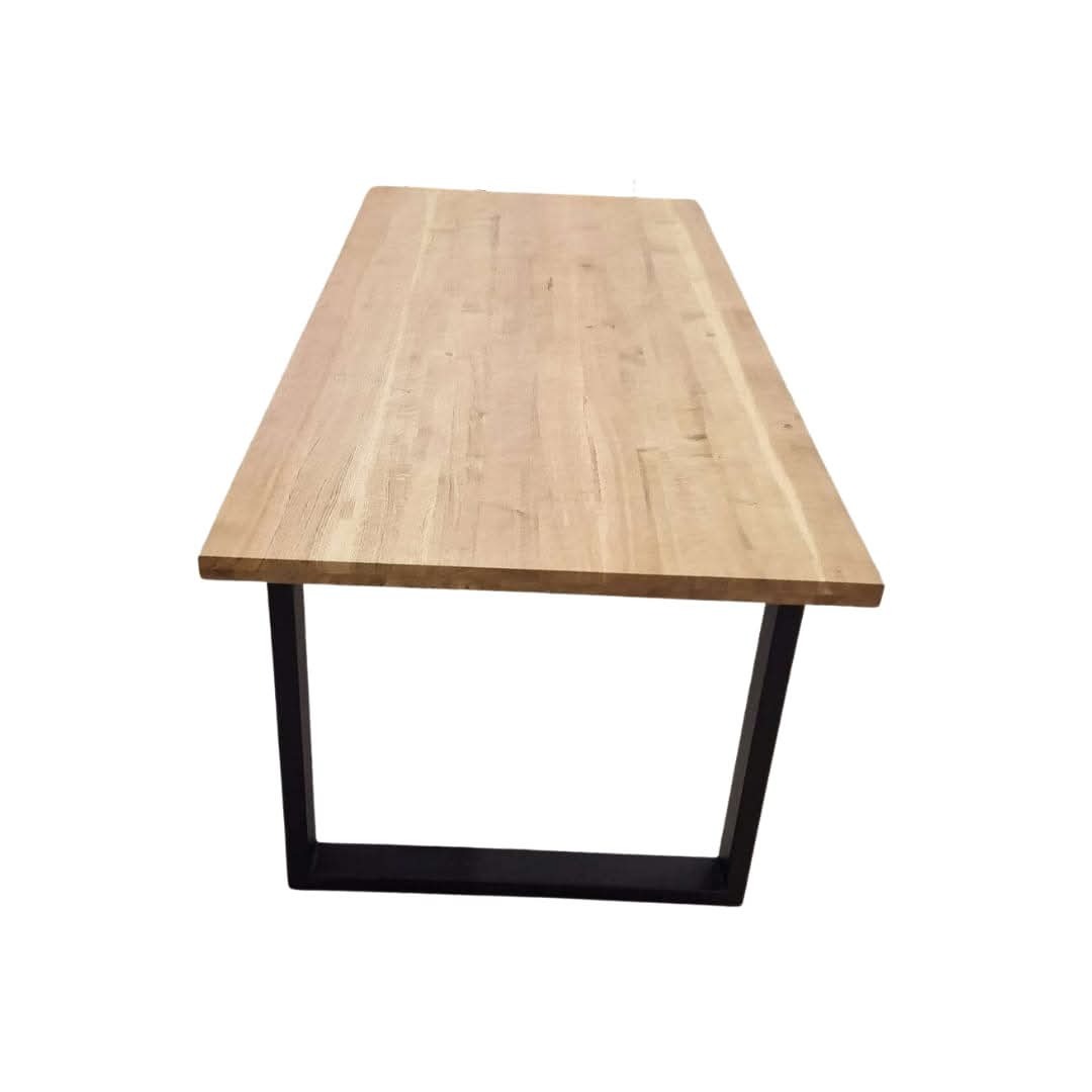 Stół z jasnego drewna o prostokątnym blacie i czarnych, metalowych nogach w kształcie litery U. Minimalistyczny design, surowe wykończenie drewna.