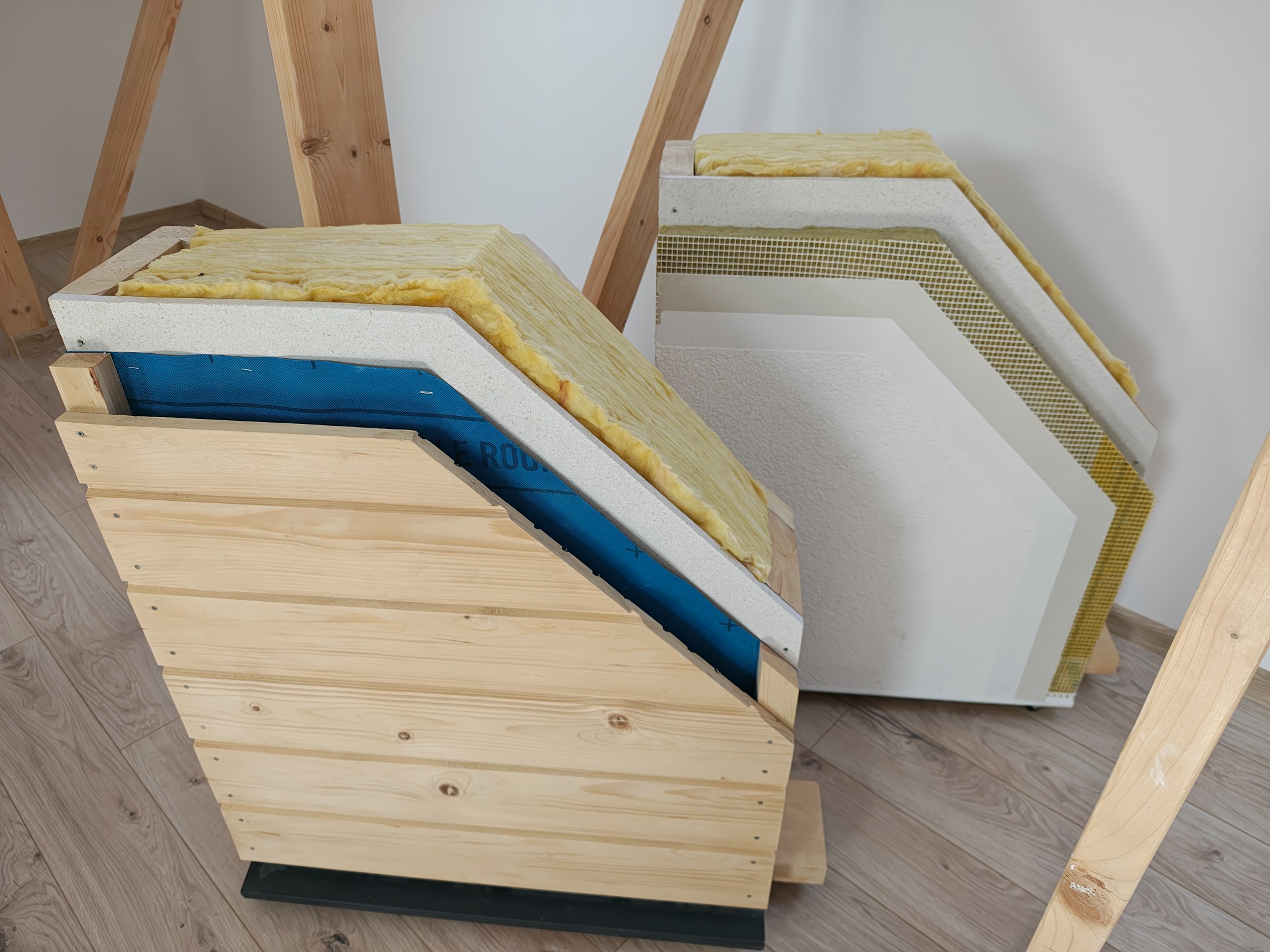 Przekrój warstw domu szkieletowego z widoczną izolacją, płytą OSB i drewnianą elewacją. Prezentacja materiałów i technologii budowlanej.