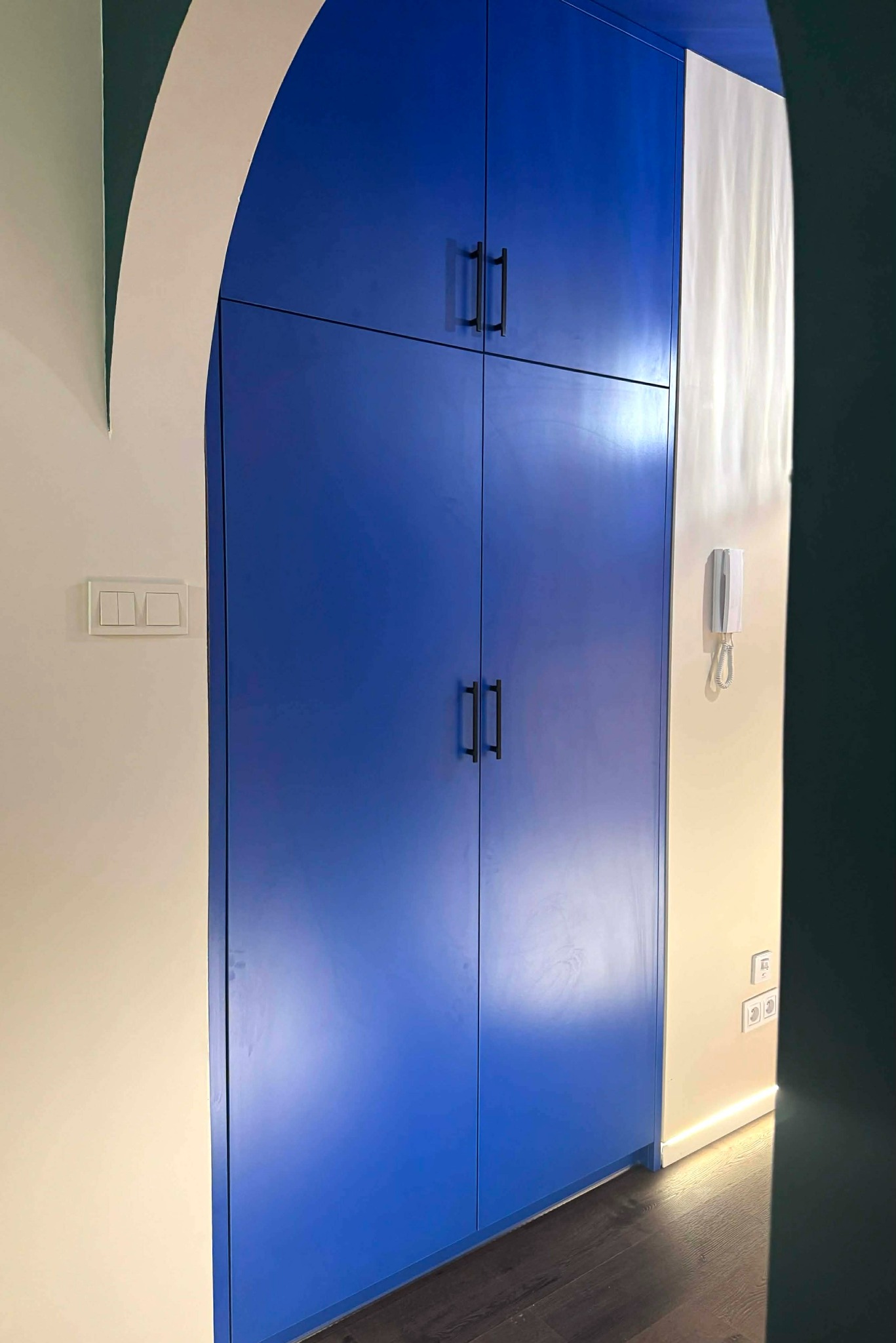 Niebieska szafa wnękowa z czarnymi uchwytami, wkomponowana w łukowate przejście, Siedlec. Nowoczesny design i funkcjonalne rozwiązanie do przechowywania.