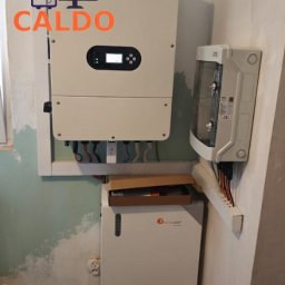 Caldo - Zamontowany inwerter i magazyn energii przy ścianie z widocznymi kablami. Na ścianie widoczny ubytek farby.
