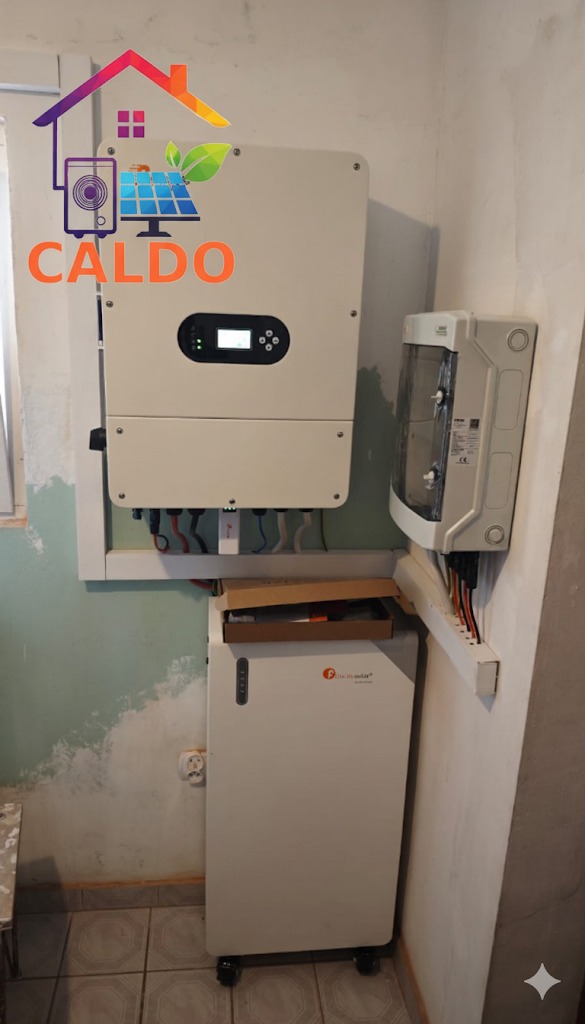 Zamontowany inwerter i magazyn energii przy ścianie z widocznymi kablami. Na ścianie widoczny ubytek farby.