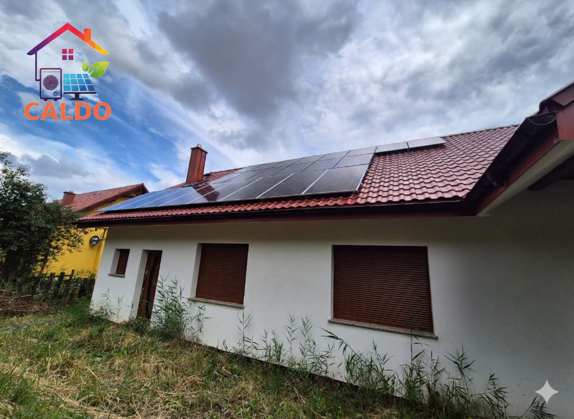 Dom jednorodzinny z instalacją paneli fotowoltaicznych na czerwonym dachu. Widoczne brązowe rolety okienne i logo firmy w lewym górnym rogu.