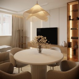 Architektura Wnętrz Aleksandra Łabuda - Jasne wnętrze z okrągłym stołem i kwiatami. W tle telewizor, regał z podświetleniem i drapak dla kota. Całość utrzymana w beżowej kolorystyce.