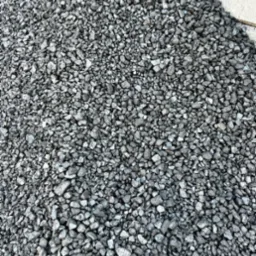 G&oacute;ra błyszczącego, szarego ekogroszku na betonowej powierzchni. Drobne, nieregularne bryłki węgla tworzą zwartą, jednolitą masę. Widok z g&oacute;ry.