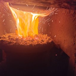 Artex Kinga Rożek - Płonący ekogroszek w piecu, z widocznymi iskrami i intensywnym, pomarańczowym płomieniem. Wnętrze pieca o nierównej, ceglanej strukturze.