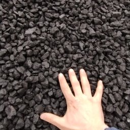 Artex Kinga Rożek - Dłoń na tle czarnego, błyszczącego węgla. Ręka wskazuje na jakość i strukturę opału, prezentując jego naturalny wygląd i właściwości.