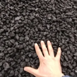 Dłoń na tle czarnego, błyszczącego węgla. Ręka wskazuje na jakość i strukturę opału, prezentując jego naturalny wygląd i właściwości.