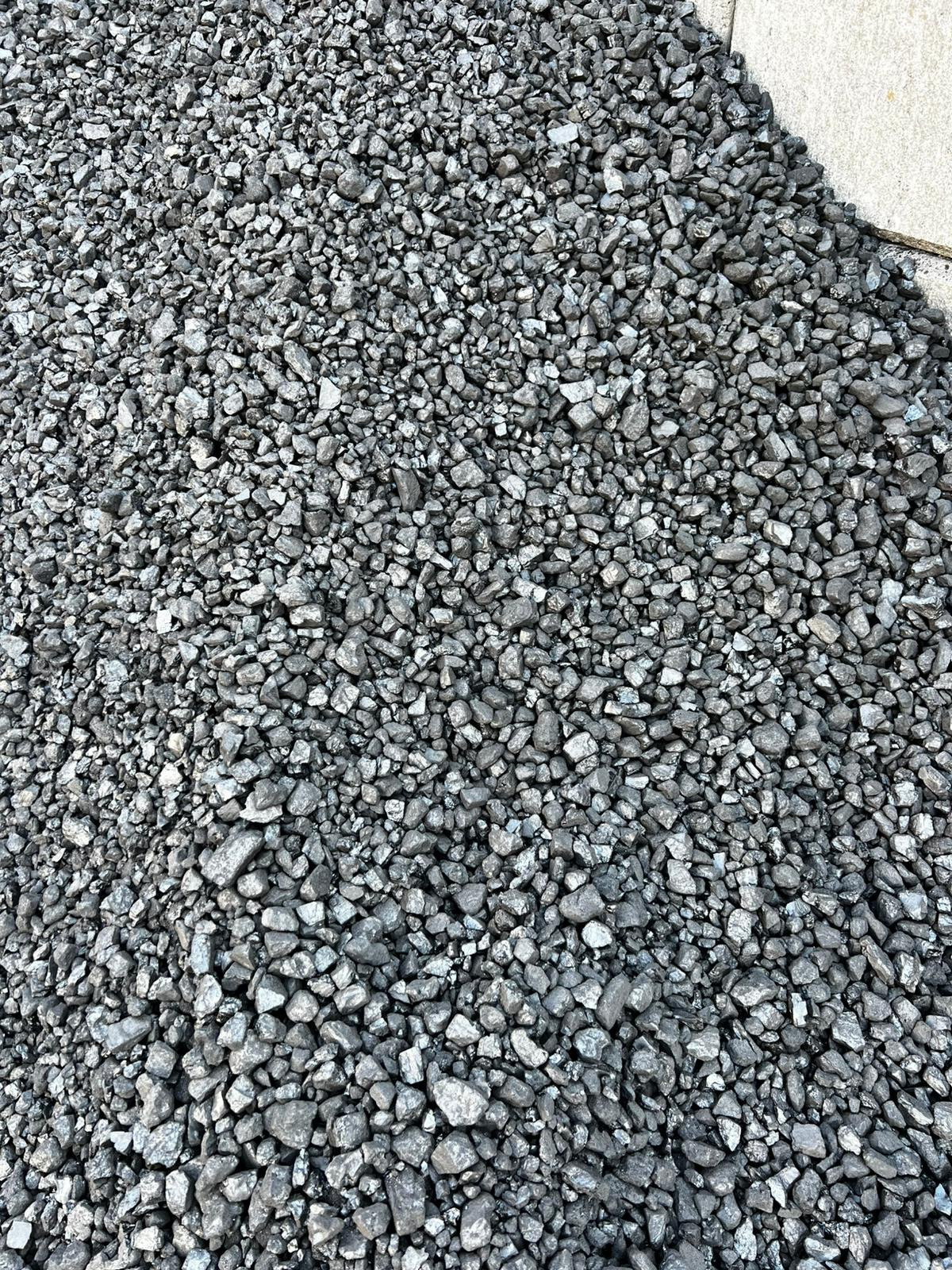 Góra błyszczącego, szarego ekogroszku na betonowej powierzchni. Drobne, nieregularne bryłki węgla tworzą zwartą, jednolitą masę. Widok z góry.