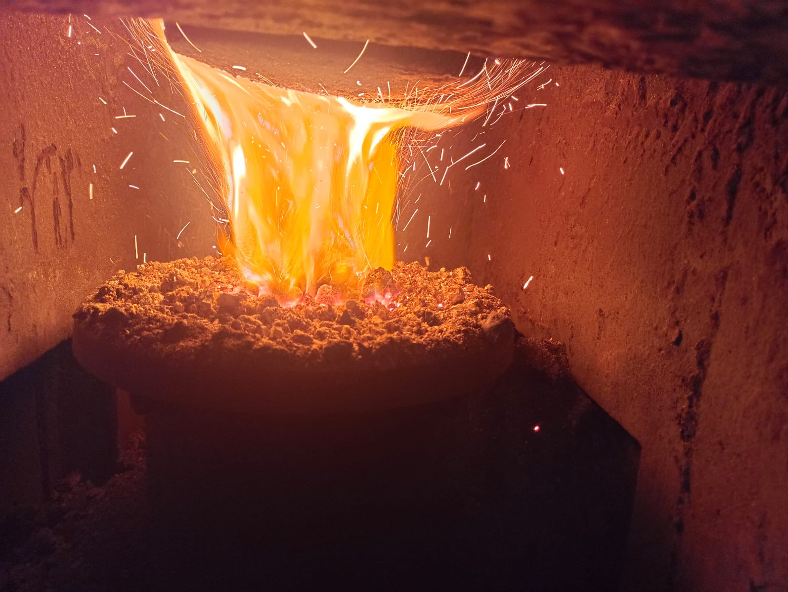 Płonący ekogroszek w piecu, z widocznymi iskrami i intensywnym, pomarańczowym płomieniem. Wnętrze pieca o nierównej, ceglanej strukturze.