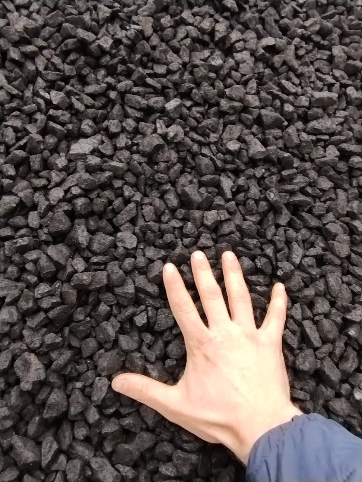 Dłoń na tle czarnego, błyszczącego węgla. Ręka wskazuje na jakość i strukturę opału, prezentując jego naturalny wygląd i właściwości.