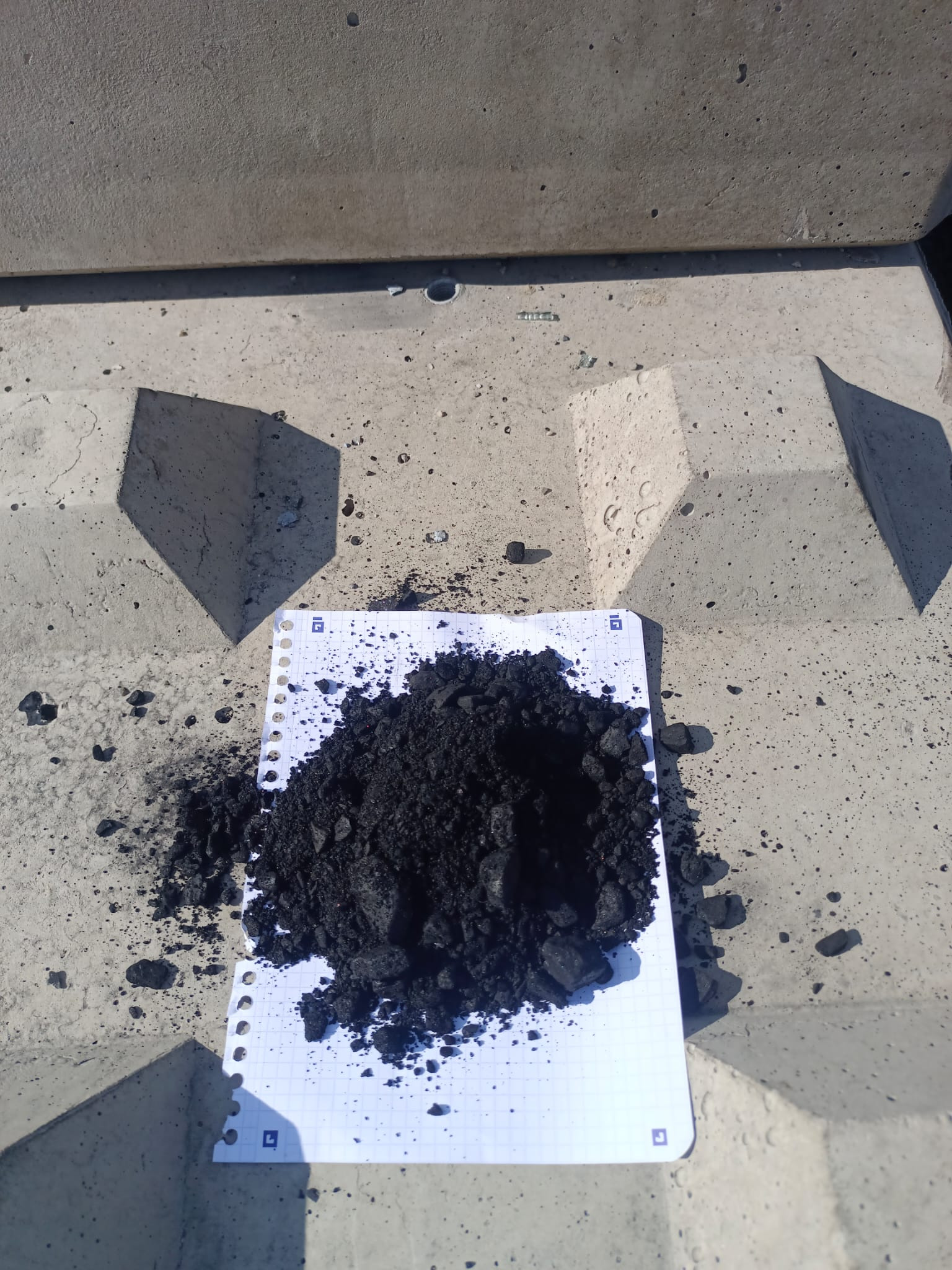 Kupa czarnego miału na kartce w kratkę, leżącej na betonowym podłożu z cieniem. Widok z góry, ostre światło.