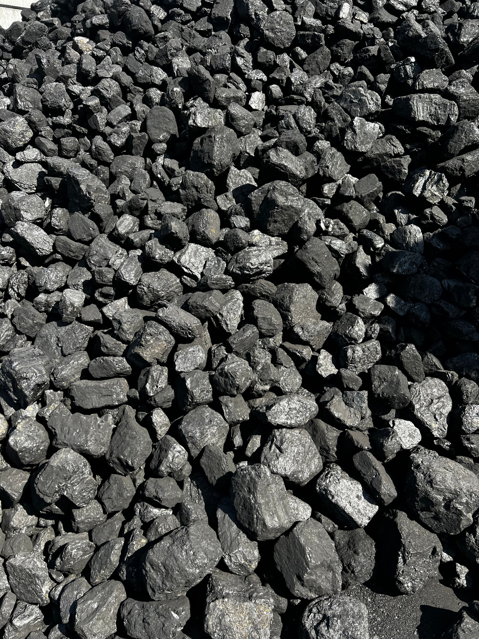 Góra błyszczącego, czarnego węgla kamiennego o nieregularnych kształtach, oświetlona naturalnym światłem słonecznym, z wyraźną fakturą i detalami poszczególnych brył.