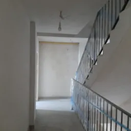 Klatka schodowa w trakcie prac wykończeniowych: ściany po tynkowaniu, posadzka wylewana, barierki schodowe zabezpieczone folią. Widok z dołu schodów.