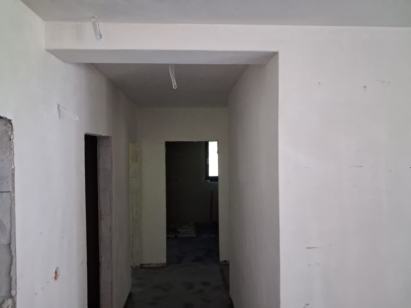 Wnętrze po pracach murarskich w Tarnowie: gładkie, białe ściany i przygotowane otwory drzwiowe. Widoczne przewody elektryczne na suficie, ściany gotowe do malowania.