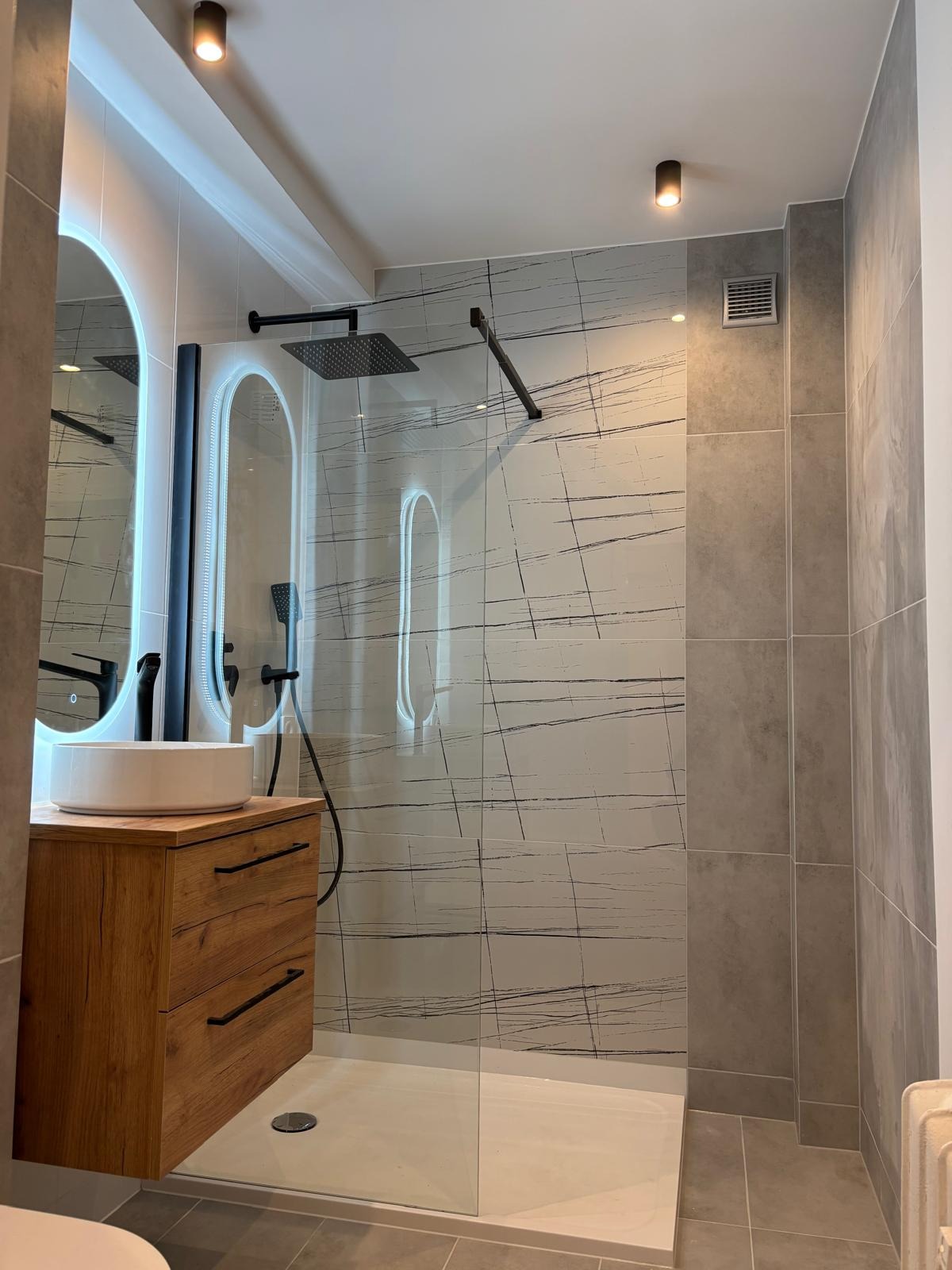 Nowoczesna łazienka po remoncie: drewniana szafka z umywalką, kabina prysznicowa ze wzorzystymi płytkami, lustro z podświetleniem LED.
